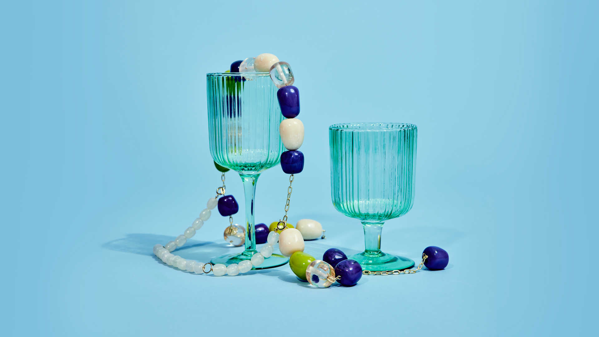 blå glas med chunky perlesmykker på og blå baggrund