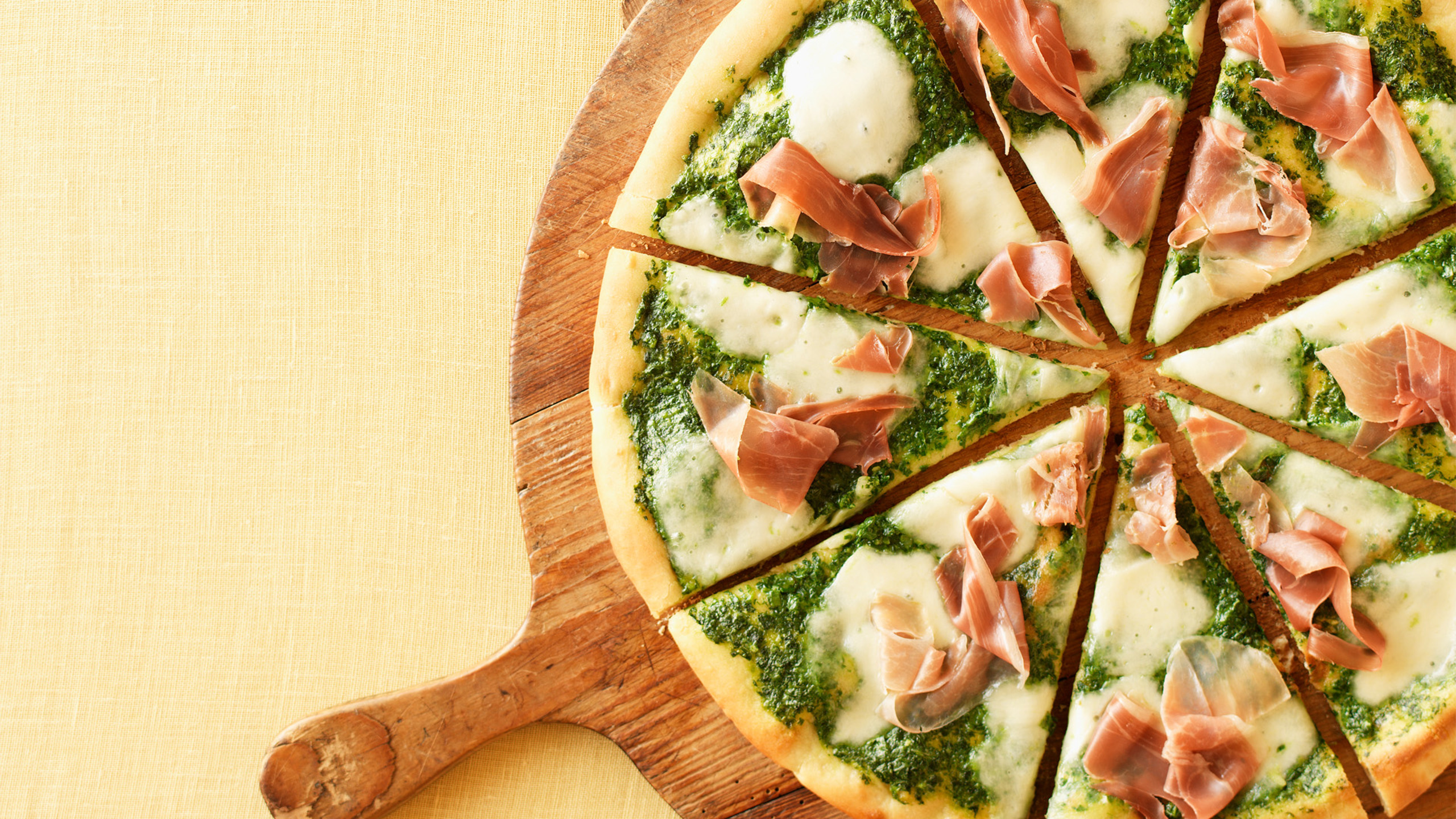 Pizza skåret ud på rundt skærebræt på gul dug